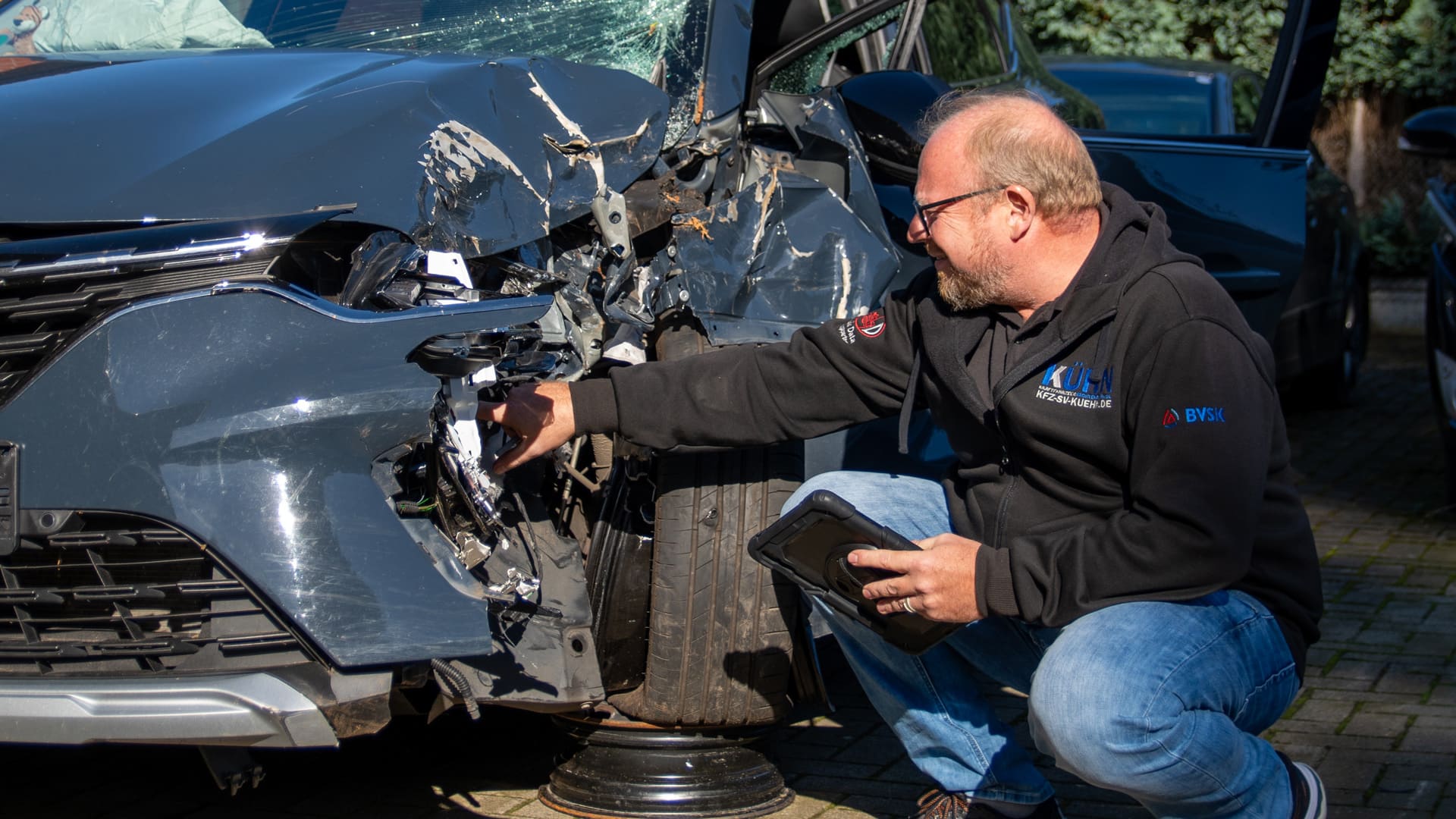 Kfz-Sachverständiger begutachtet mit einem Tablet den Frontschaden eines Unfallfahrzeugs