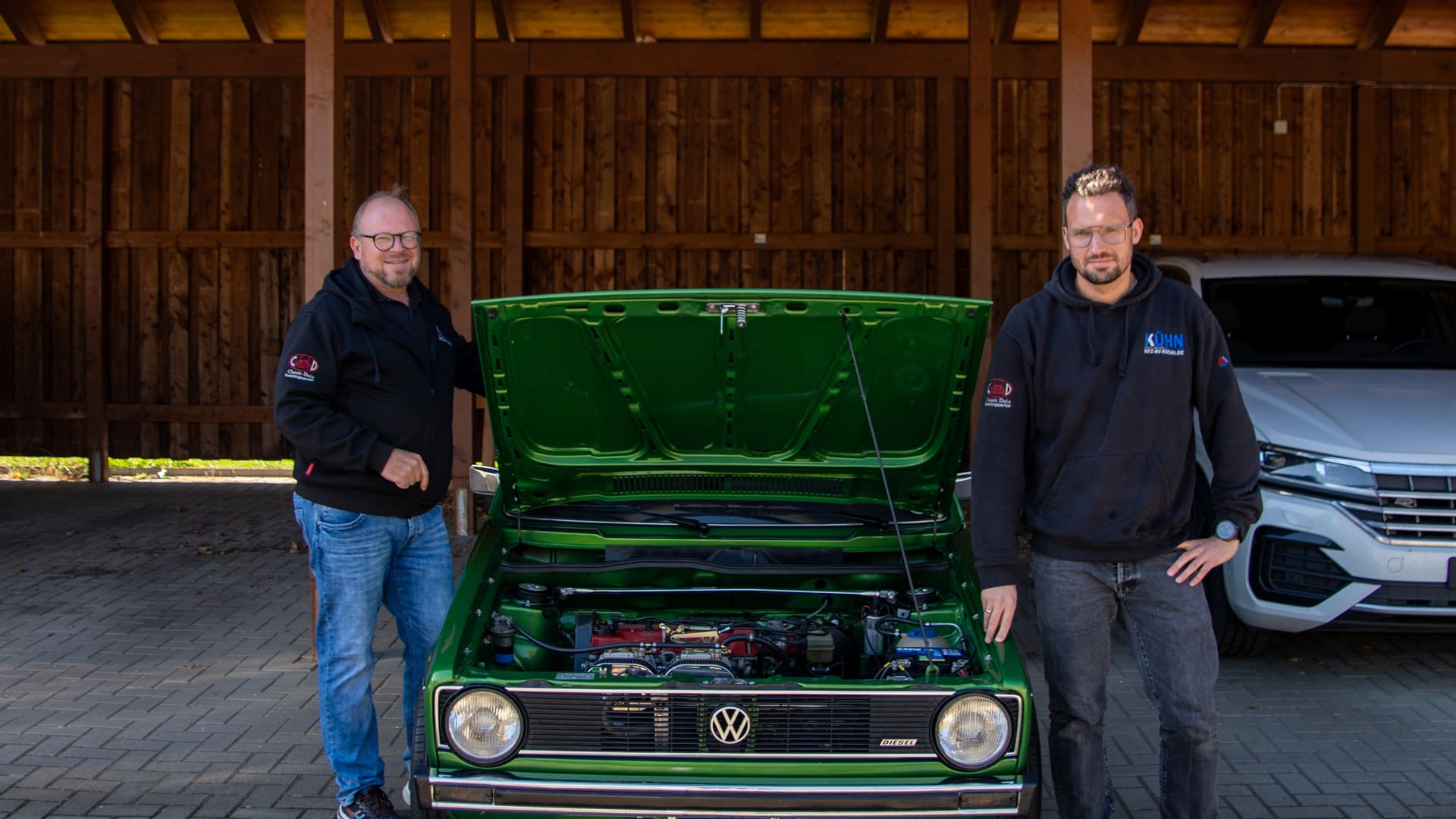 Karsten Kühn und Daniel Korfsmeier neben einem grünen VW Golf mit geöffneter Motorhaube